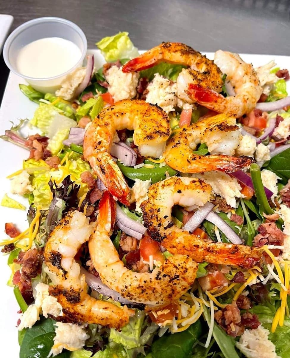 Seafood Cobb salad topped with seasoned grilled shrimp, crabmeat, red onion, tomato, bacon and shredded cheese, with dressing in a cup on the side